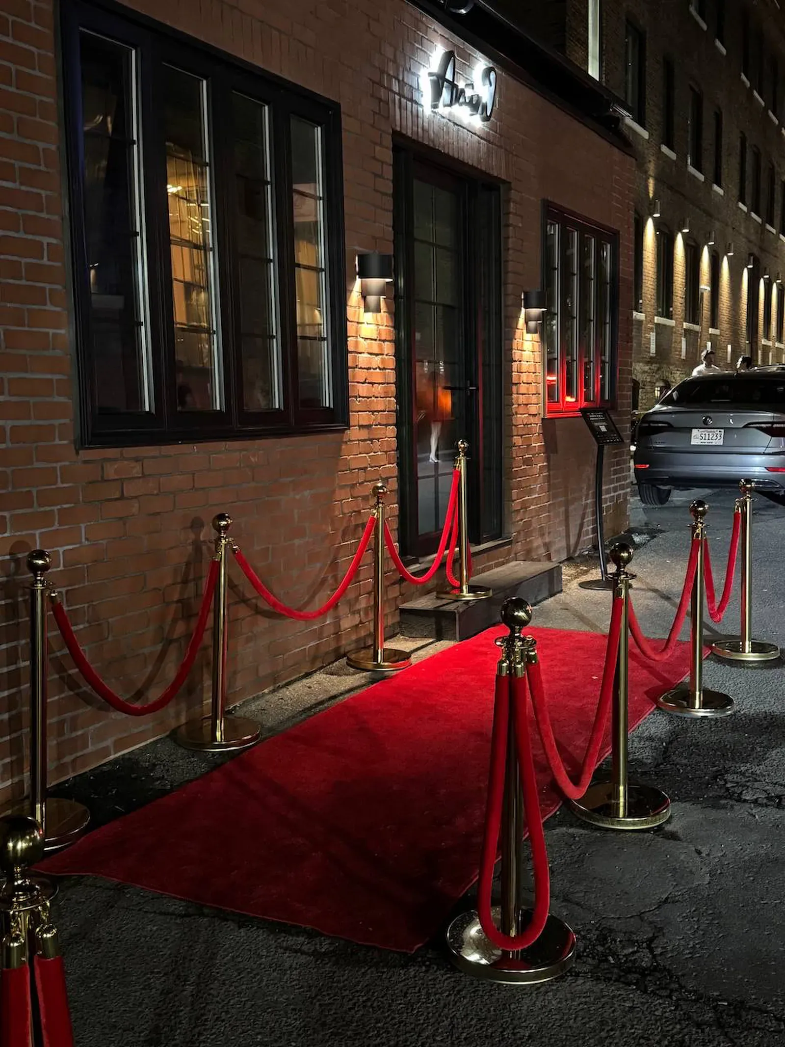 Poteaux à corde dorés avec cordes de velours rouges à côté d’un tapis rouge, à une entrée en soirée